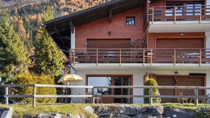 A two-story wooden chalet with a balcony, a dining area, and a view of a forested mountain. - Pigne 1 by Interhome (Verbier)