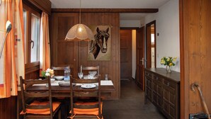 A wooden dining area with a table set for four, chairs with orange cushions, a hanging light fixture, and a horse-themed wall hanging. - Pigne 1 by Interhome (Verbier)