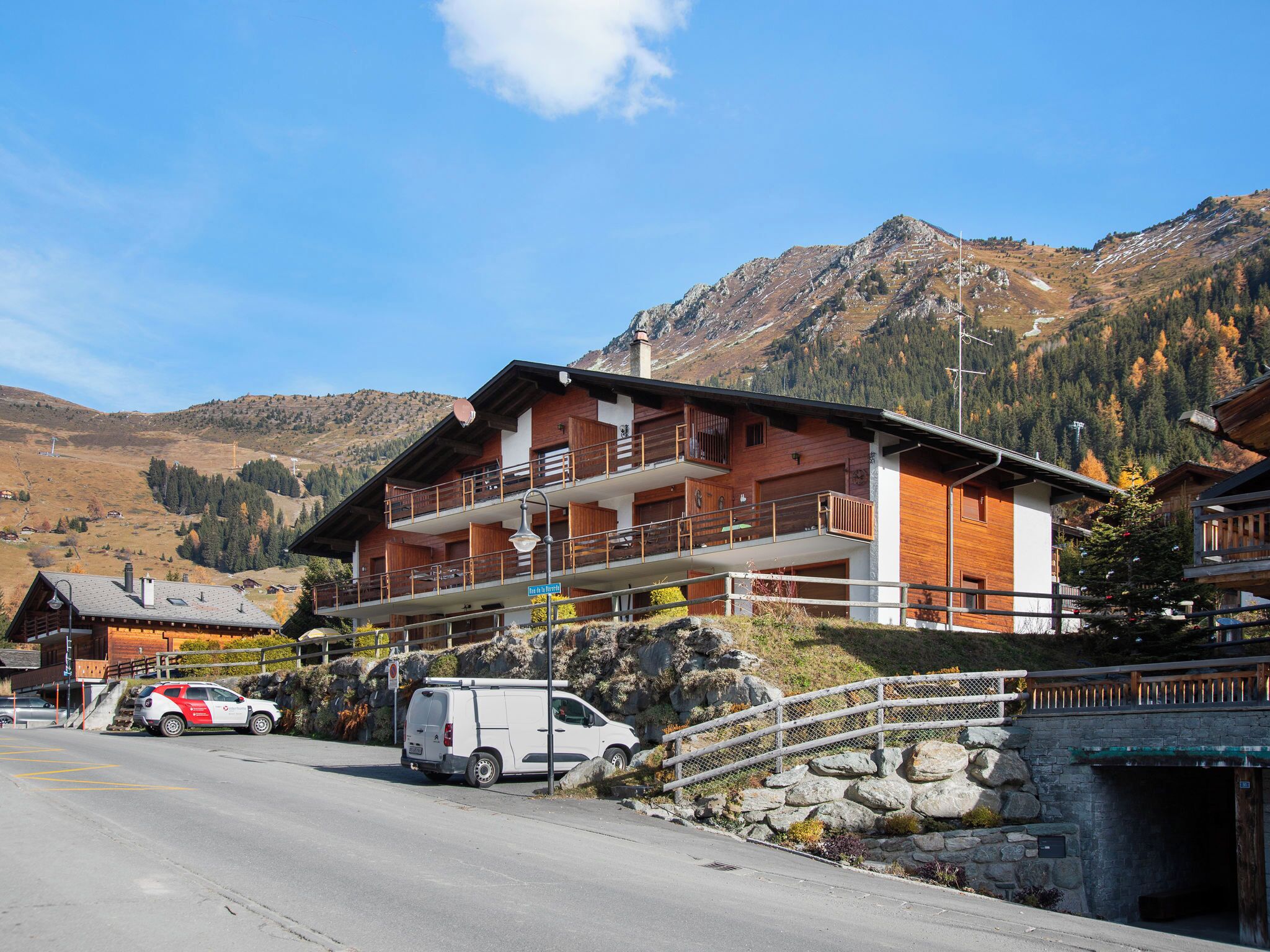 Ein zweistöckiges Holzhaus mit Balkonen, einer Steinsäule und einem Blick auf die Berge.