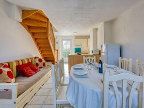 Um quarto aconchegante com sofá, mesa de jantar, cadeiras e uma escada de madeira.