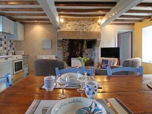 Un coin repas chaleureux avec une cheminée en pierre, des poutres en bois et un téléviseur en arrière-plan.