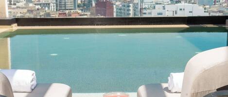 A rooftop pool with two lounge chairs and a table, a martini glass, and sunglasses on the table.