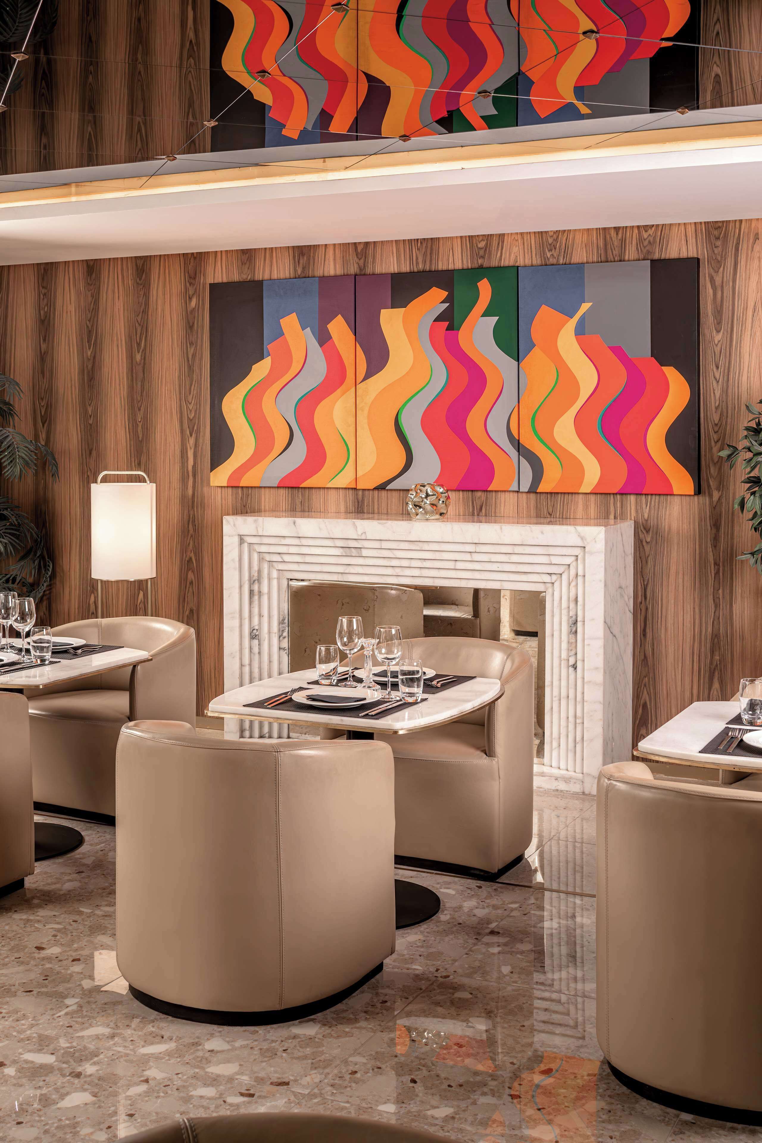 Un área de comedor moderna con mesas redondas, sillas color beige y una chimenea.