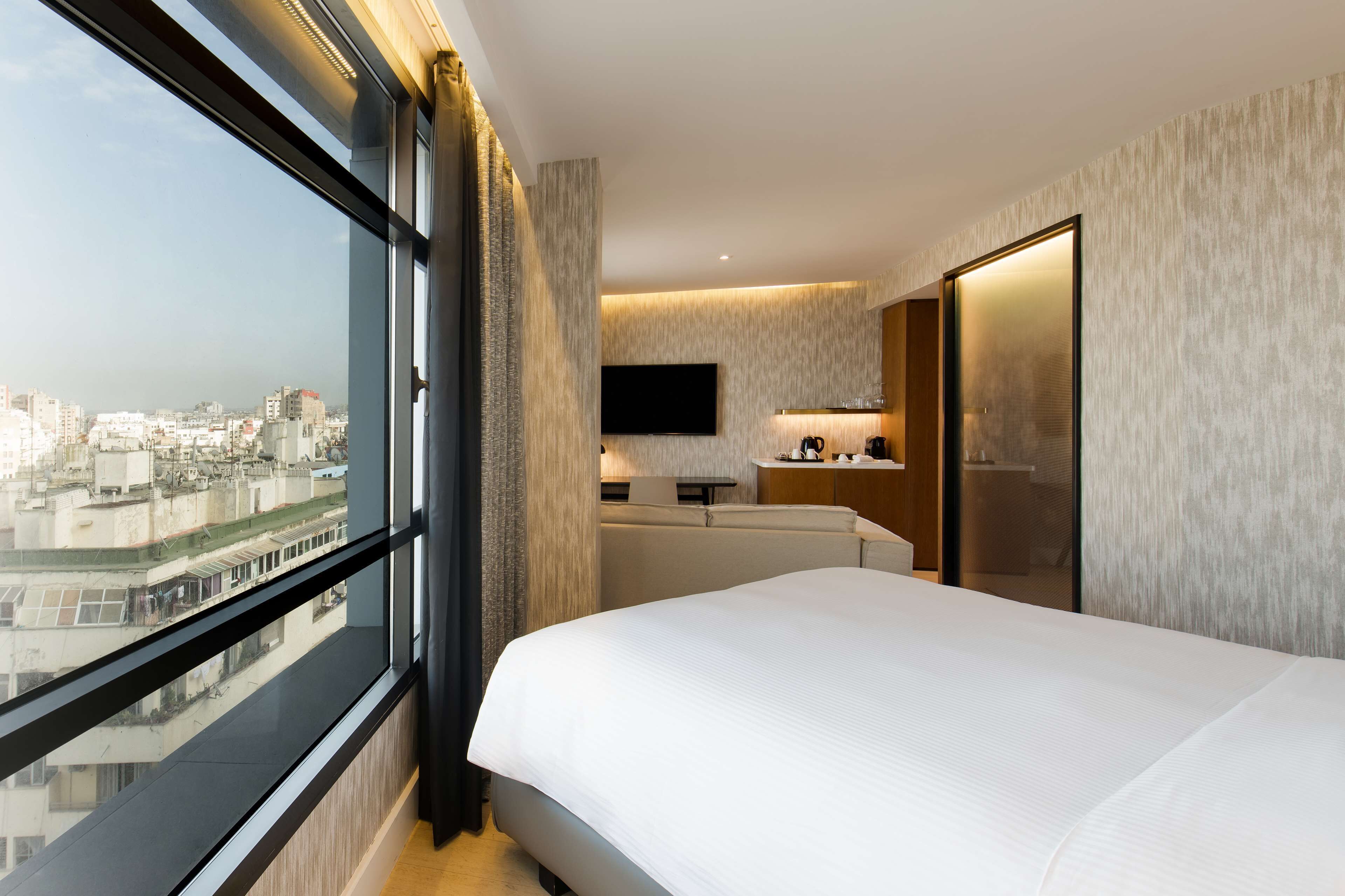 Een moderne hotelkamer met een groot bed, een televisie, een kleine kitchenette en uitzicht over de stad.