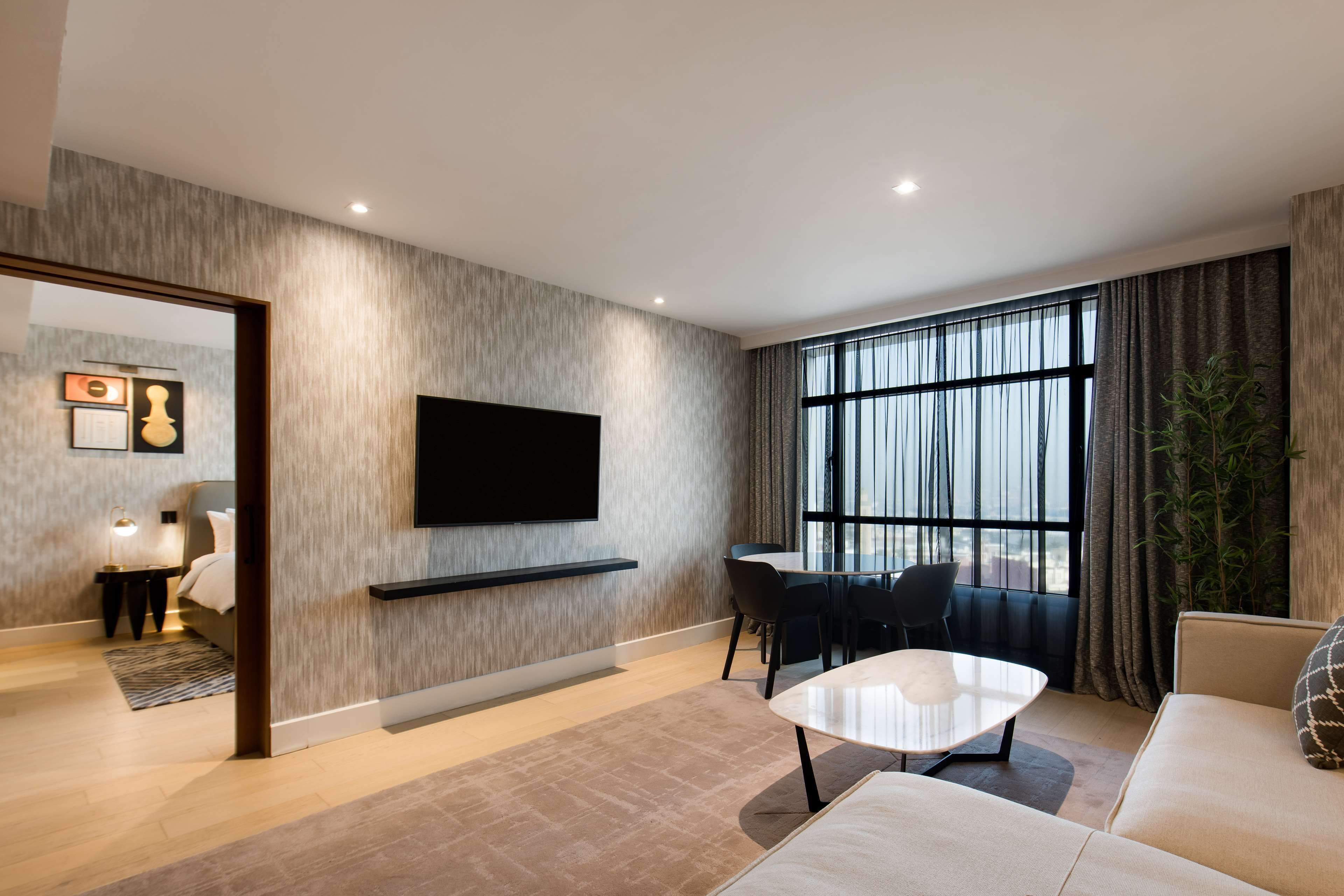 Ein modernes Wohnzimmer mit einem an der Wand befestigten Flachbildfernseher, einer Couch, einem Couchtisch und einem Essbereich mit Stühlen.