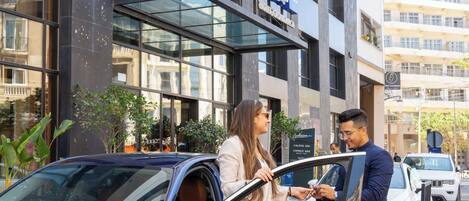 Fachada de vidrio moderna de un hotel, un letrero que dice 'Hotel Casbah' y un BMW estacionado al frente.