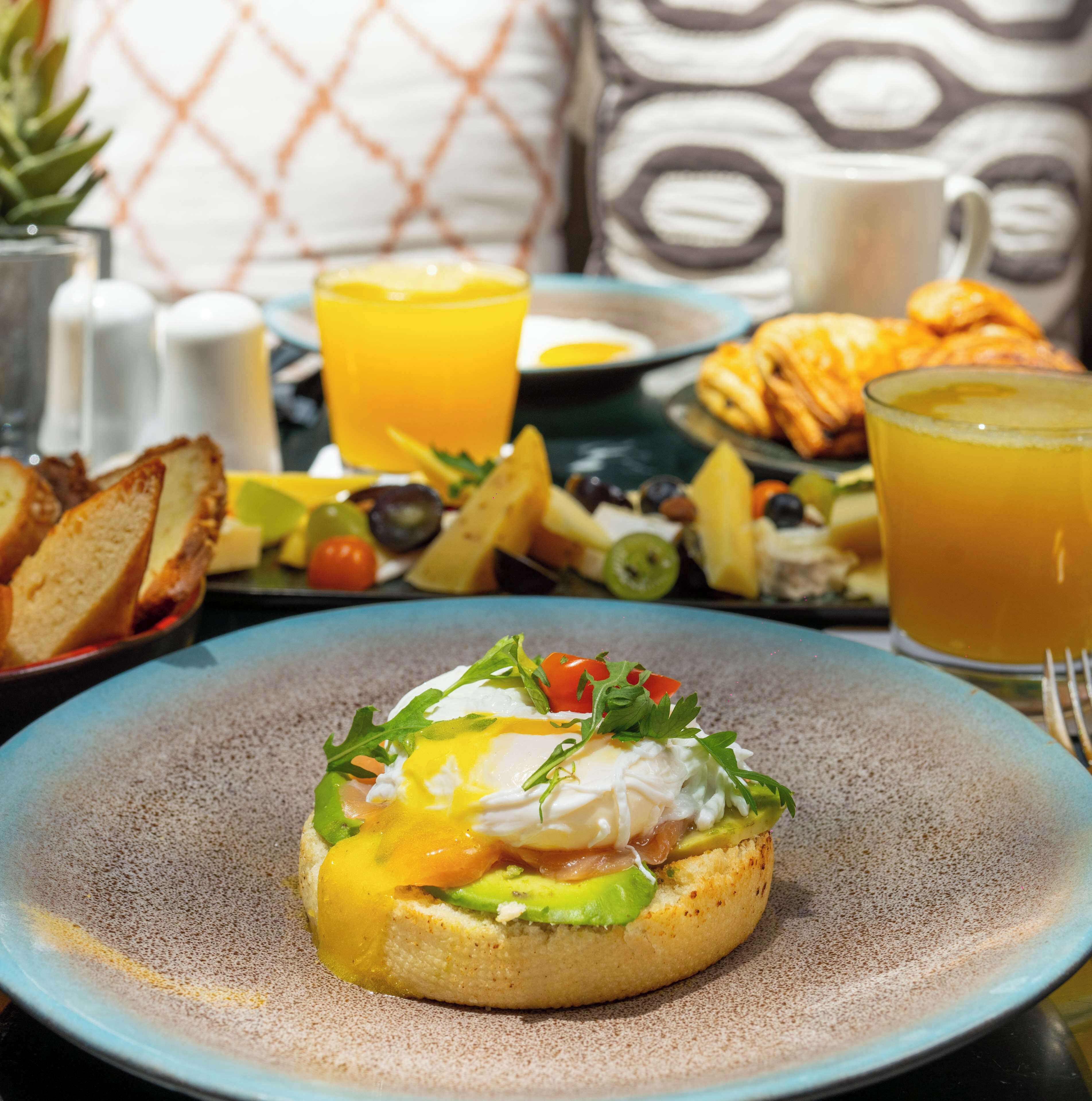 Une table mise pour le petit-déjeuner avec un œuf poché sur une tranche de pain grillé, un verre de jus d’orange et une assiette de croissants.