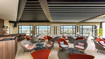 A modern lounge area with multiple seating options, a bar, and large windows offering city views.