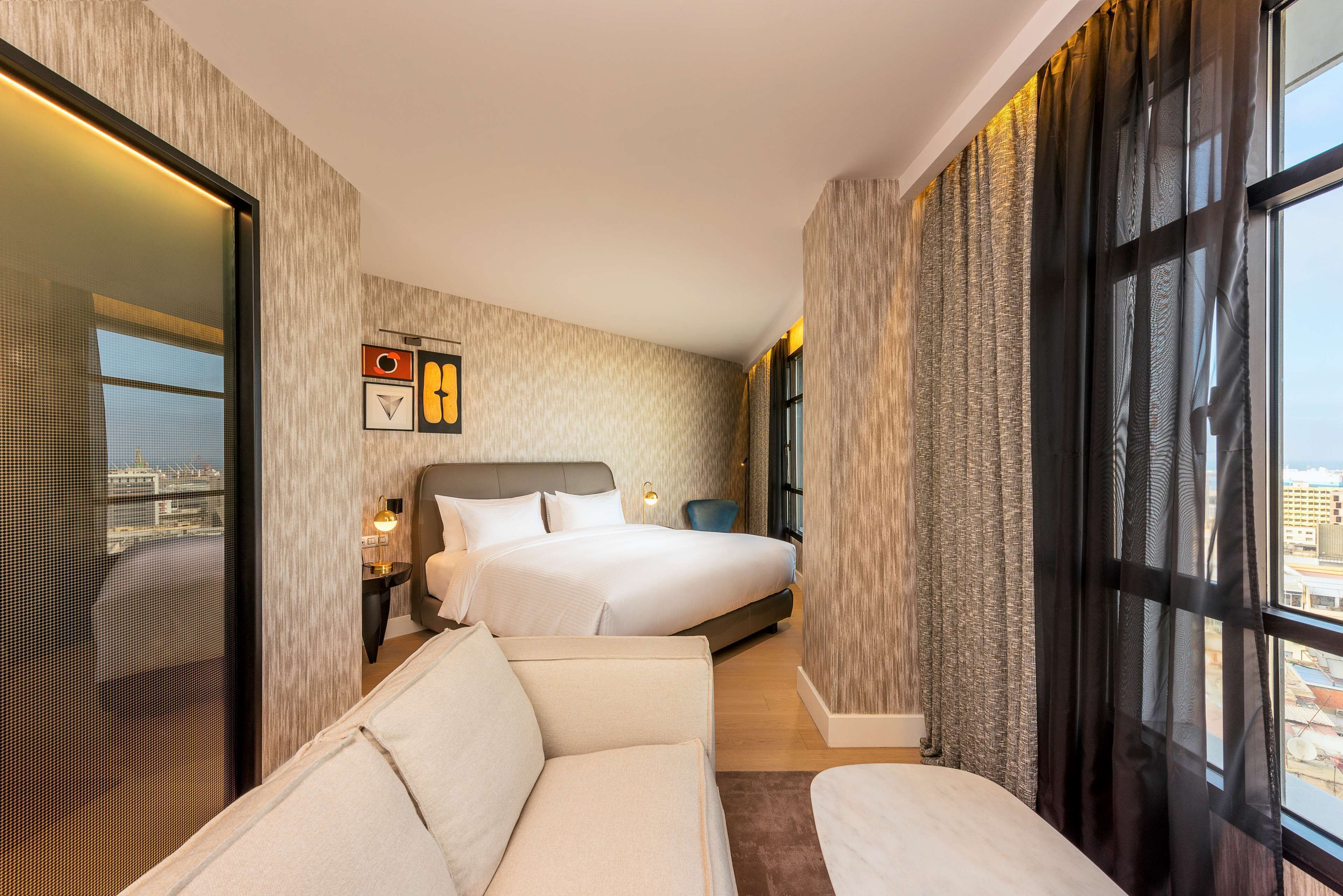Une chambre d’hôtel avec un grand lit, un canapé, une table de chevet et une fenêtre avec des rideaux.