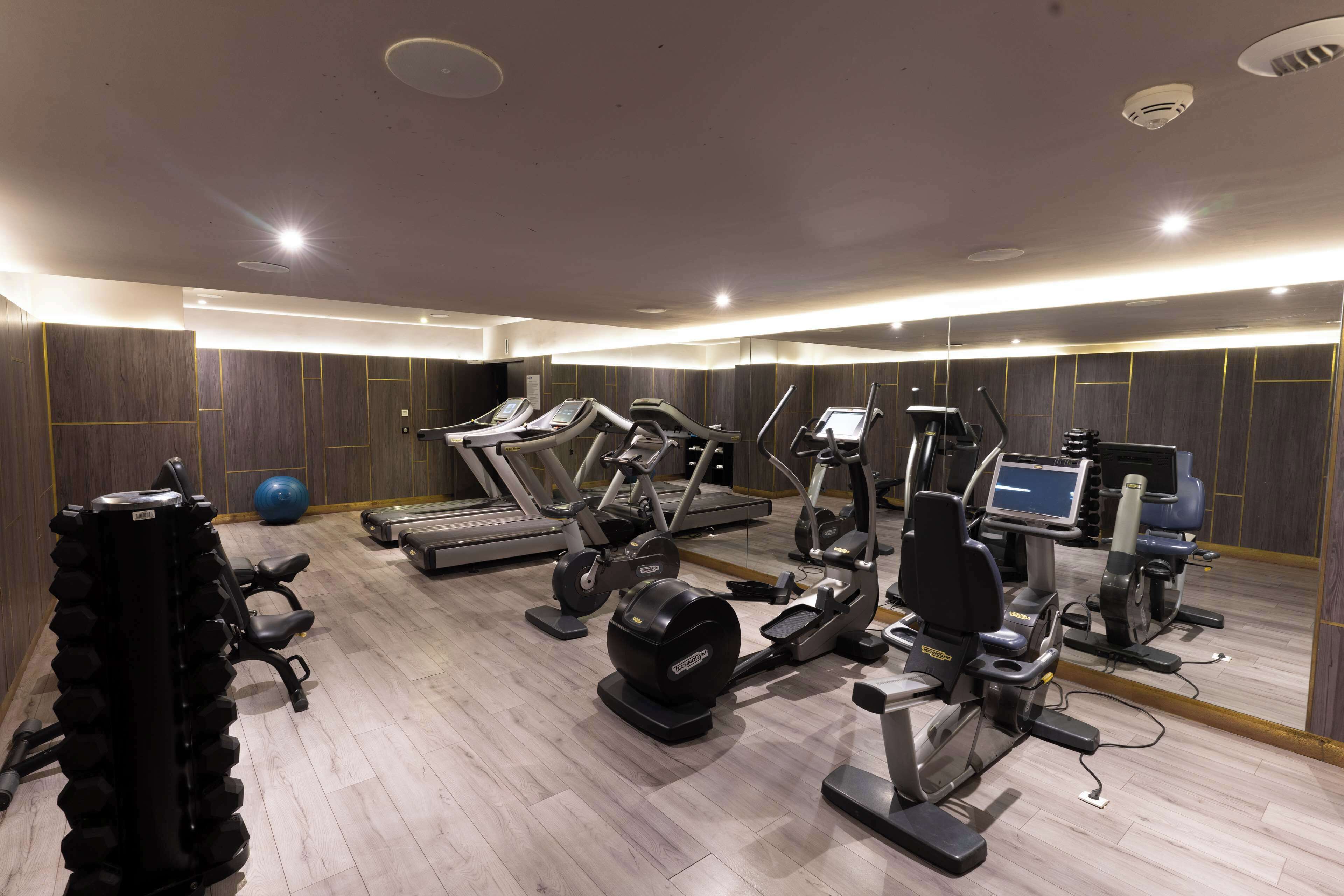 A modern gym with various cardio and strength training equipment, including treadmills, elliptical machines, and free weights.