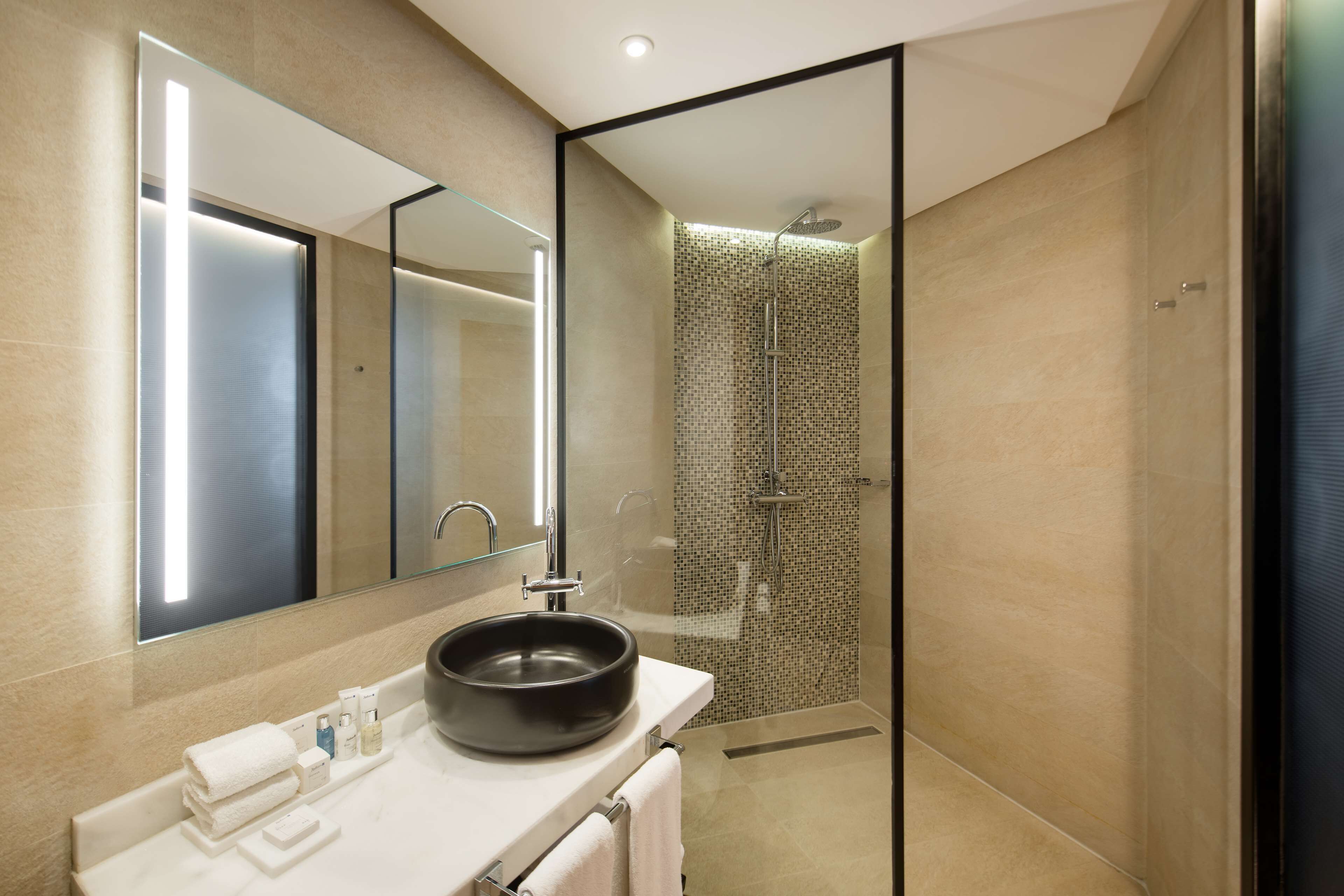 Un baño moderno con un espejo grande, un lavabo redondo y una ducha con mampara de vidrio.