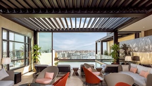 Un salón moderno con vistas a la ciudad, que incluye sofás, sillones y una barandilla de vidrio que domina el paisaje urbano.