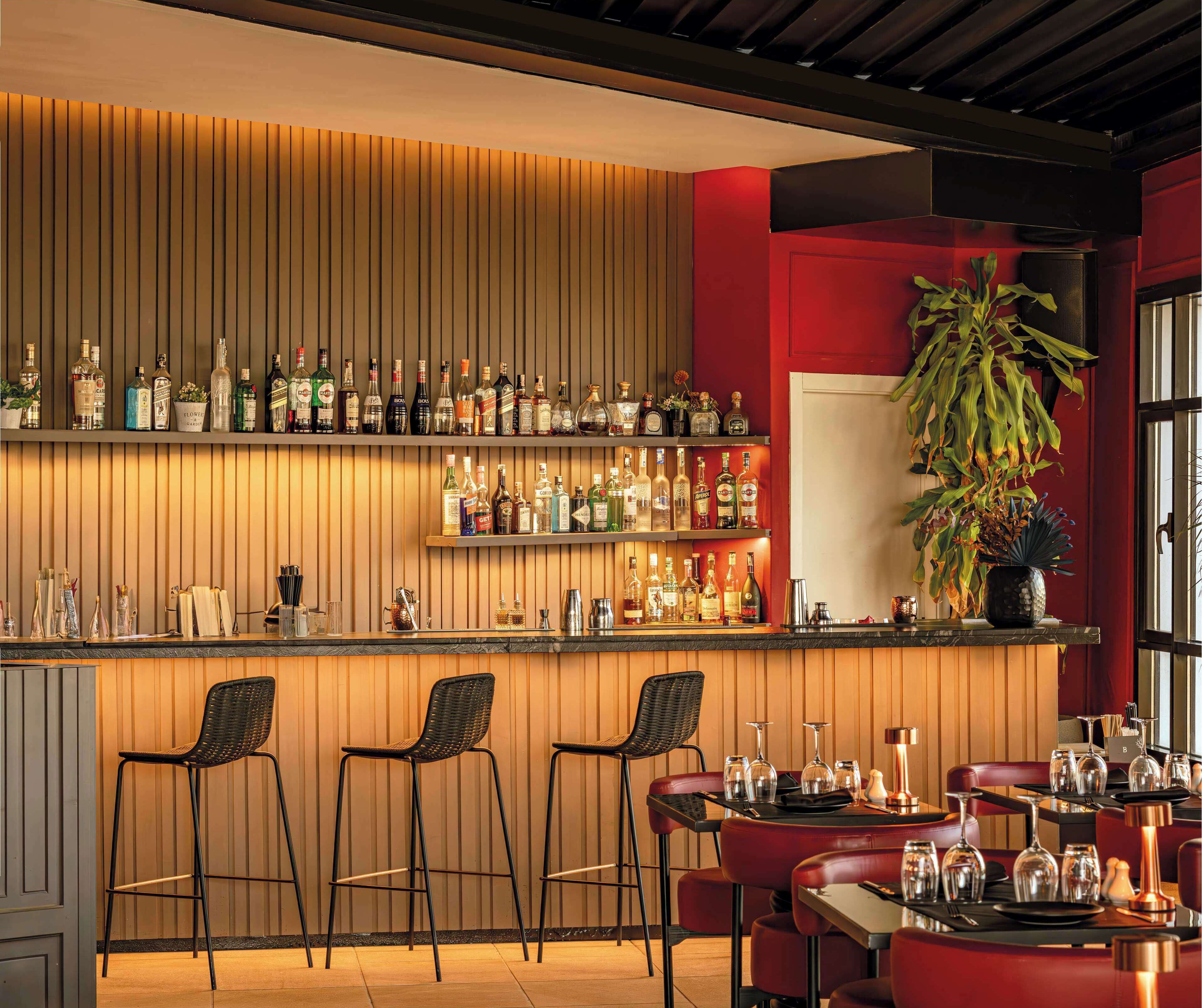 Zona de bar con listones de madera, estantes con botellas de licor y taburetes de bar.