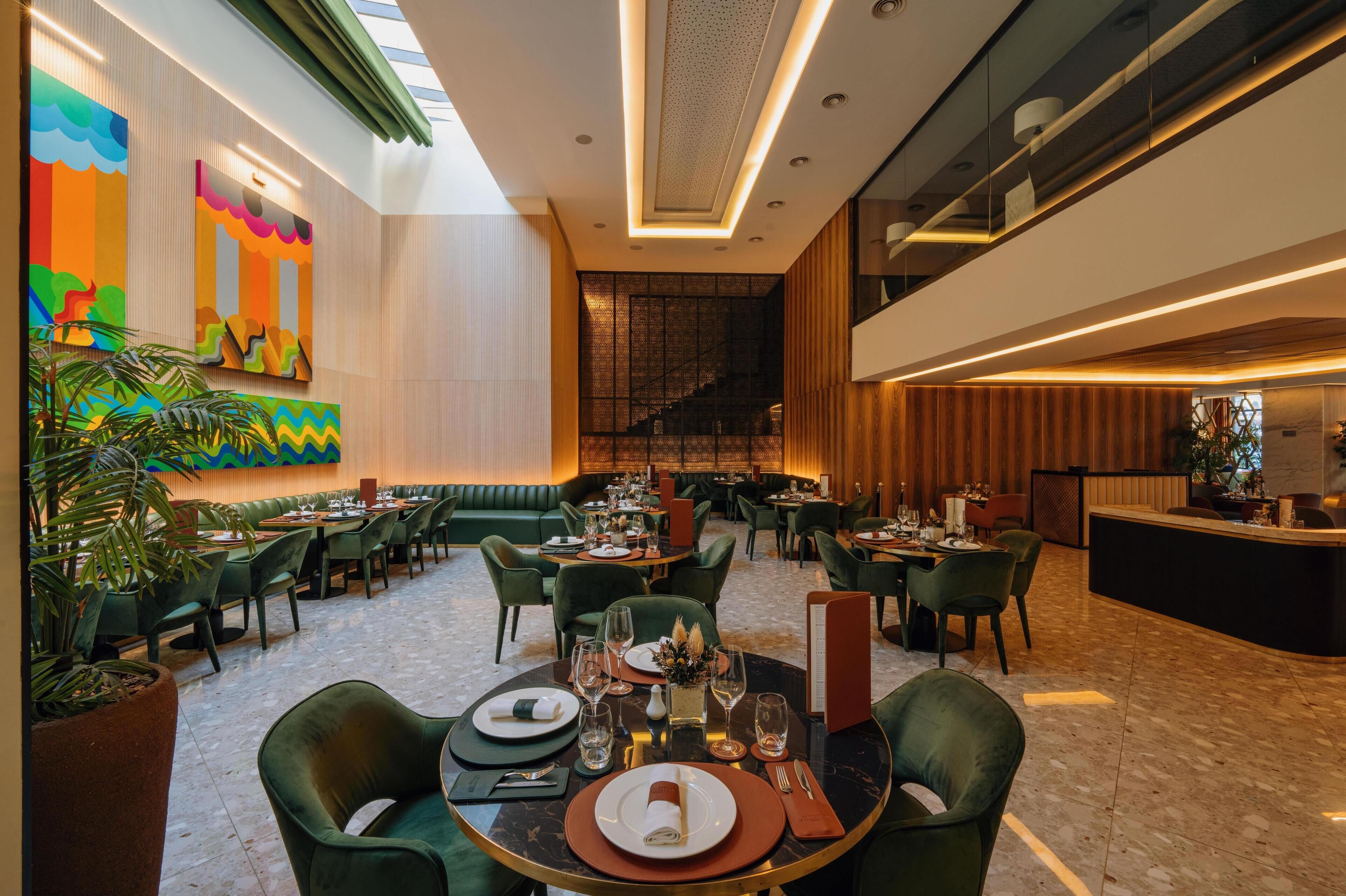 A modern dining area with green upholstered seating, a central table with a folded napkin, and a menu stand.