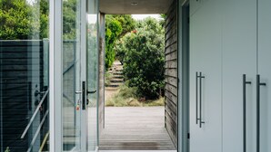 Un hall d’entrée moderne avec des portes vitrées donnant sur une terrasse en bois et un jardin.