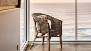 Une chaise en osier avec un coussin, dans une pièce dotée d’une grande fenêtre donnant sur l’océan.