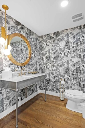 A bathroom with a patterned wallpaper, a gold-framed mirror, a white sink, and a white toilet. - 1BR, Next to Monastery Wedding Venue, w/Bathtub (Cincinnati)