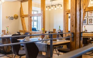 A dining area with wooden beams, tables, chairs, and a modern chandelier. - Ferienhaus Prinzessinnenturm (Blankenburg)
