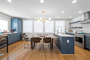 A modern kitchen with a central island, wooden flooring, and a chandelier.