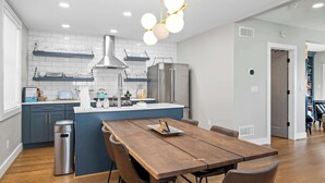 A modern kitchen with white tiles, stainless steel appliances, and a wooden dining table.