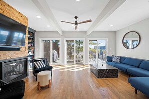 Una sala de estar moderna con chimenea, ventilador de techo y un amplio ventanal con vistas a un balcón.