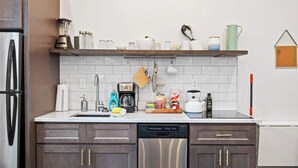 Cozinha moderna com geladeira de aço inoxidável, lava-louças e máquina de café no balcão.