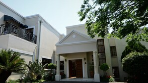A building with a white facade, a covered entrance, and a brick pathway leading to the entrance. - Highgrove Guesthouse (Sandton)