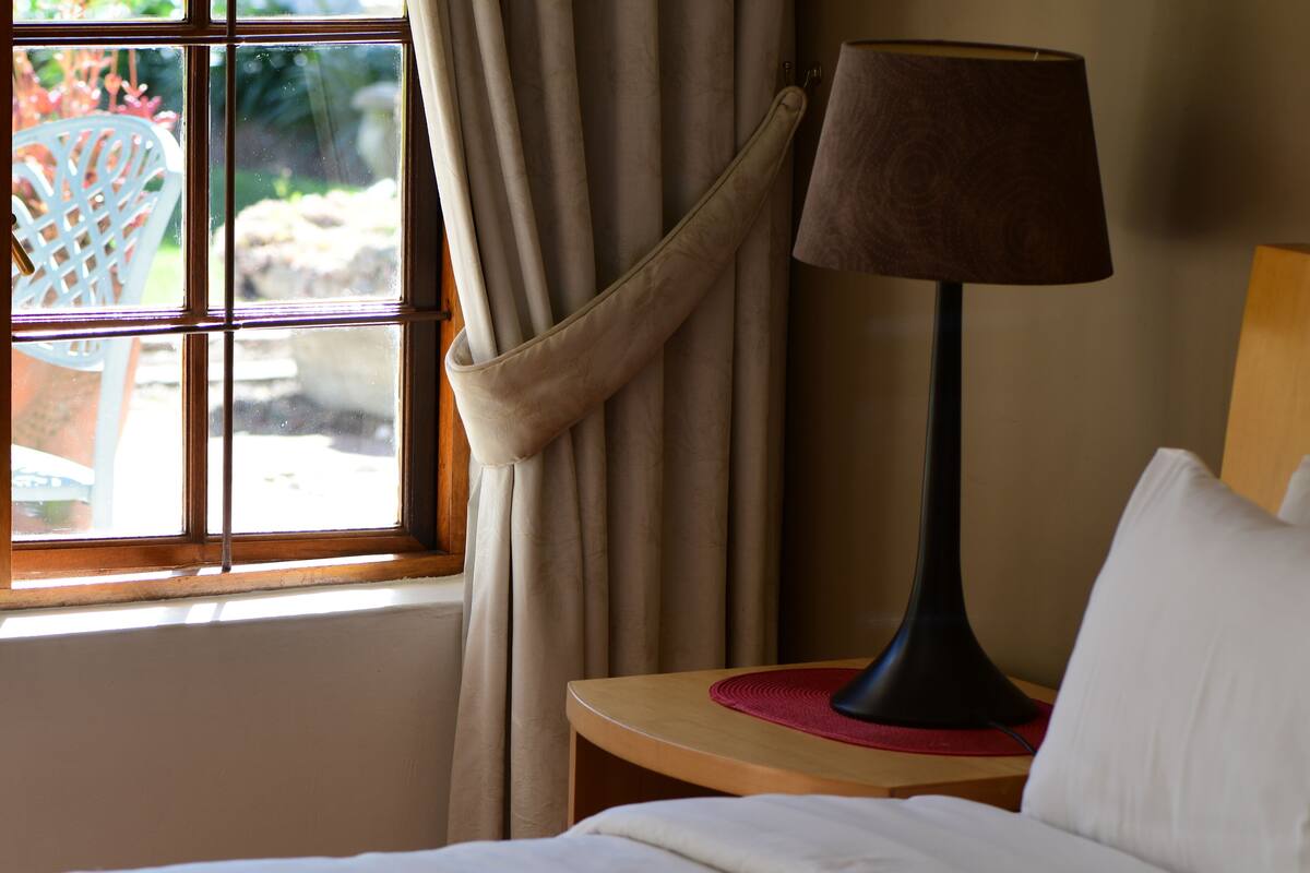 Een hotelkamer met een bed, nachtkastje met lamp, raam met gordijnen en uitzicht op de omgeving.