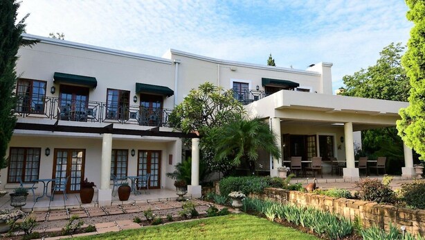A two-story building with a patio area, outdoor seating, and a well-maintained garden. - Highgrove Guesthouse (Sandton)