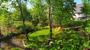 A lush garden with a small stream, wooden bridges, and a white building in the background. - Plitvice Streaming (Plitvicka Jezera)