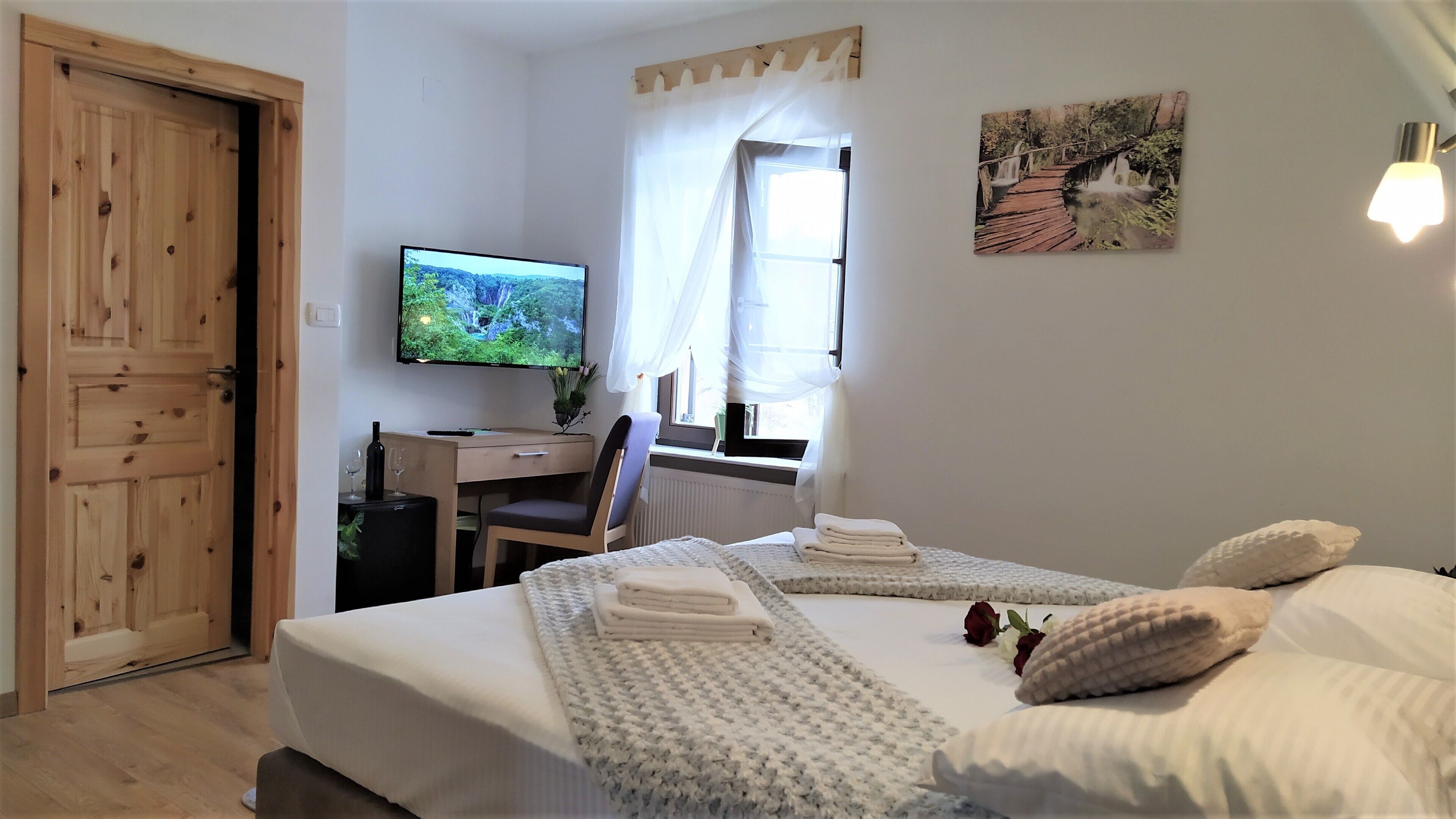 A bedroom with a bed, a desk, a television, and a window with curtains.