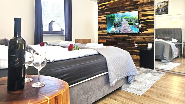 A hotel room with a bed, a TV mounted on a wooden wall, a bottle of wine, and a rose on the bed. - Plitvice Streaming (Plitvicka Jezera)