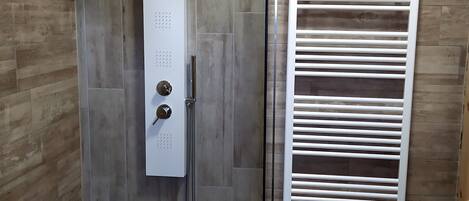 Una ducha con panel de control, puerta de cristal y toallero con una toalla.