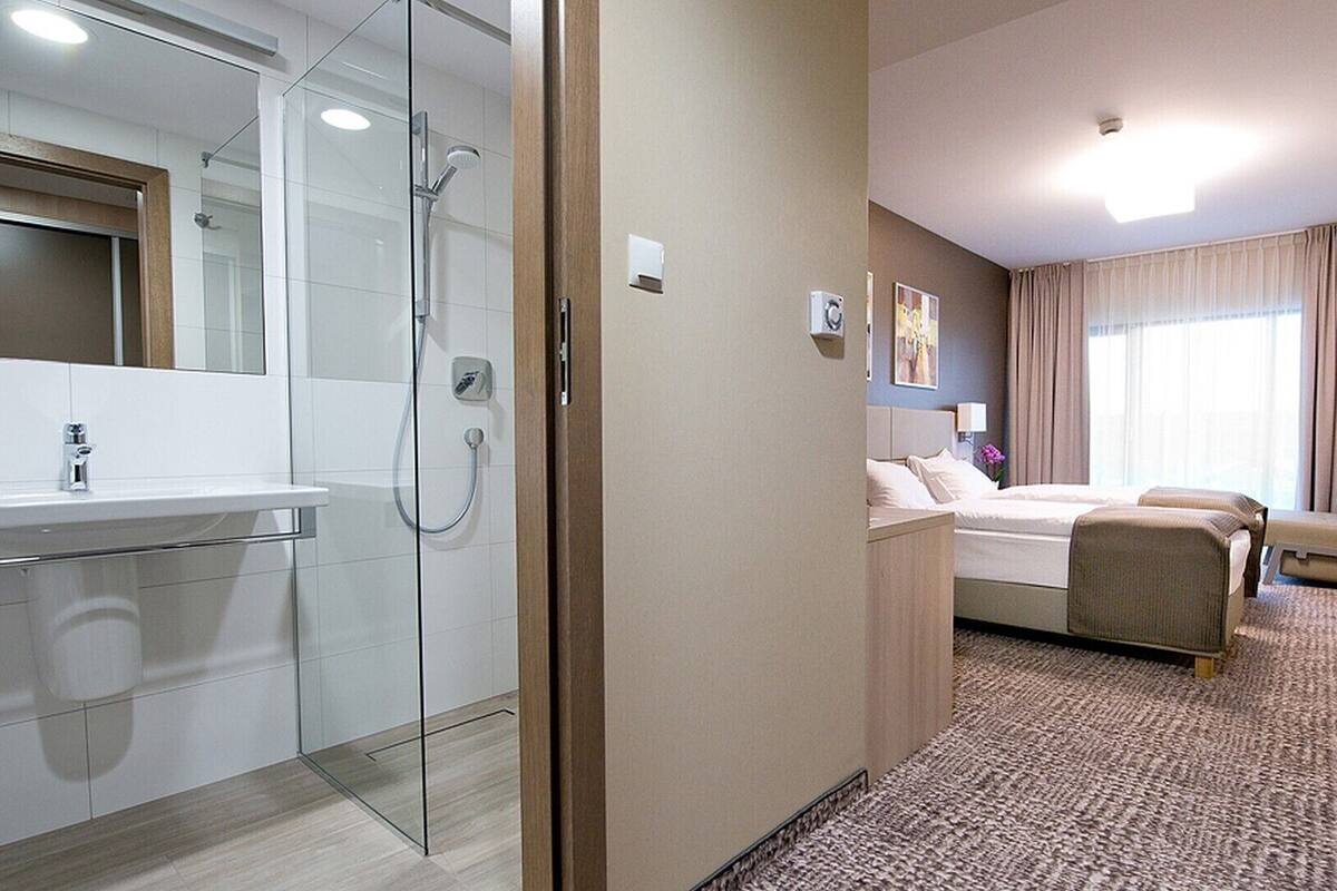 Ein Hotelzimmer mit Dusche, einem Bett, einer Sitzecke und einem Badezimmer mit Waschbecken und Spiegel.