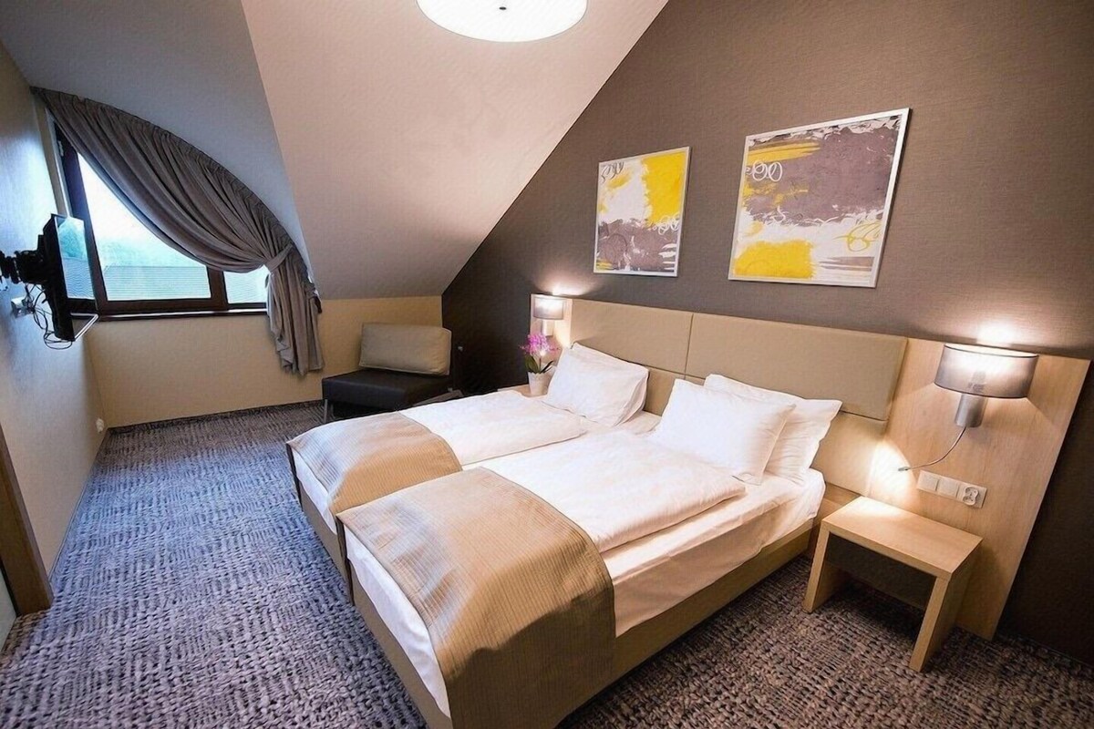 A hotel room with a large bed, bedside tables, a window with curtains, and artwork on the wall.