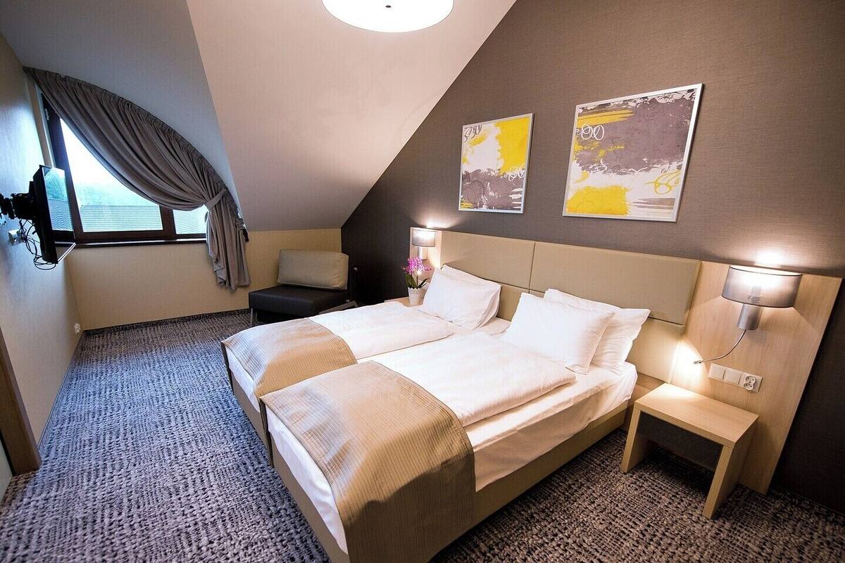 Ein Hotelzimmer mit einem großen Bett, Nachttischen, einem Schreibtisch, einem Sessel, einem Fenster mit Vorhängen und Bildern an der Wand.