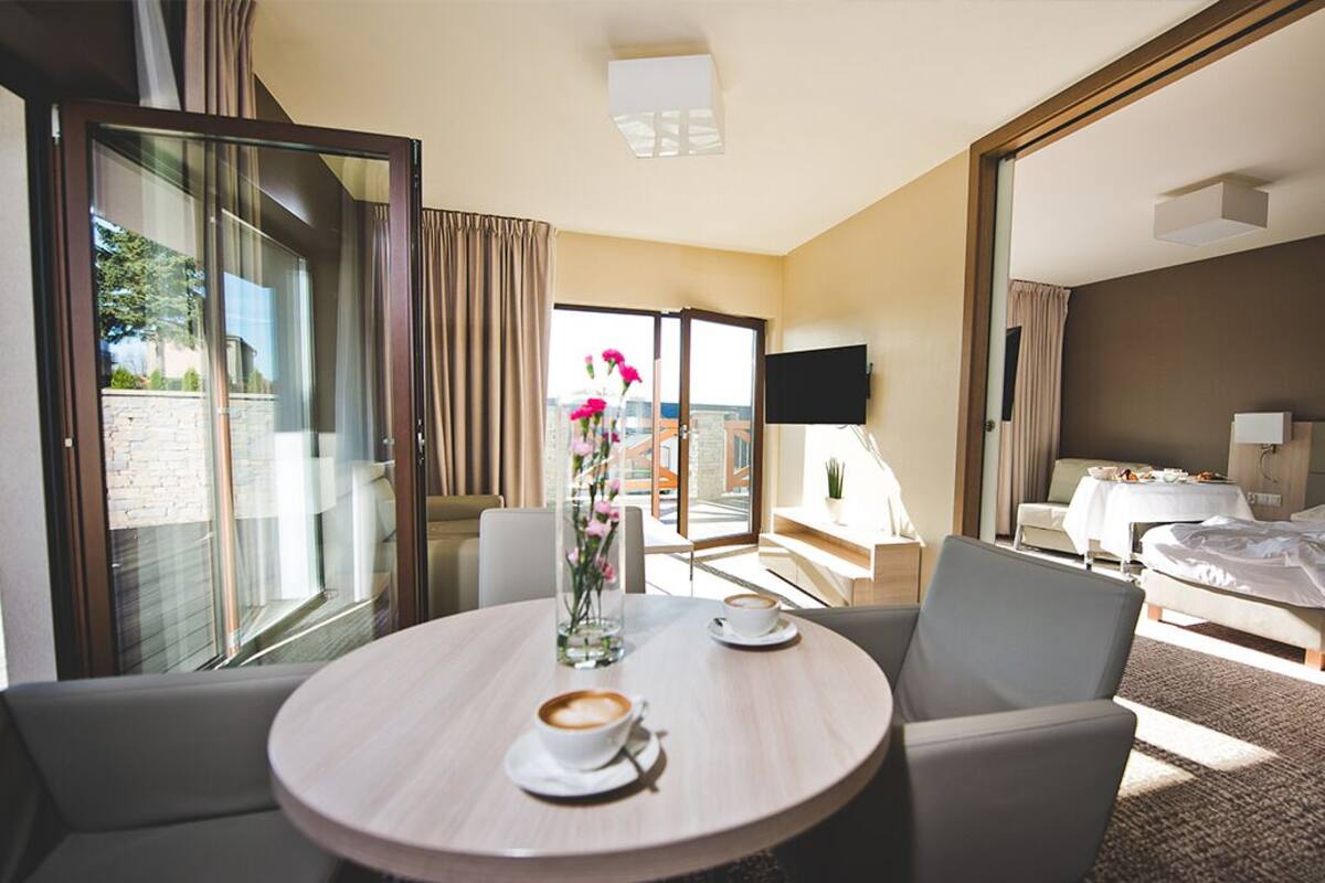 Ein Hotelzimmer mit einem runden Esstisch, zwei Stühlen, einem Bett, einem Fernseher und einem Balkon mit Blick.