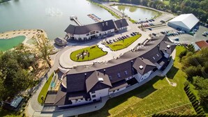 A large, modern building with a curved roof, surrounded by a parking lot and a lake. - Molo Resort Hotel (gmina Osiek)