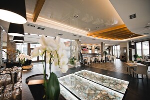 Um hall amplo com área de estar central, uma vitrine de vidro com objetos decorativos e uma escada à esquerda.