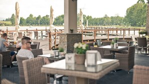 An outdoor restaurant with wicker furniture, tables, and umbrellas, overlooking a body of water. - Molo Resort Hotel (gmina Osiek)
