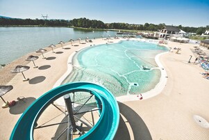 Parque aquático com uma piscina grande, toboáguas e áreas de praia com guarda-sóis.