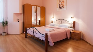 A bedroom with a bed, bedside table, nightstand, wardrobe, and a potted plant.