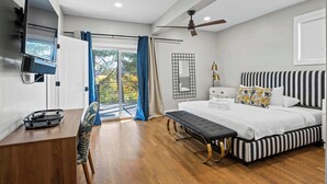 Ein modernes Schlafzimmer mit einem großen Bett, einem Schreibtisch, einem Stuhl, einem Deckenventilator und Blick durch eine Glastür.