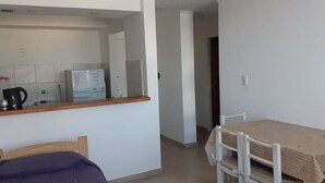 A small, clean room with a bed, a table with a tablecloth, a chair, and a kitchenette area with a refrigerator, microwave, and coffee maker. - Departamentos Balcarce (Balcarce)
