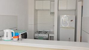 A compact kitchen with white cabinets, a gas stove, a refrigerator, and a kettle on the counter. - Departamentos Balcarce (Balcarce)