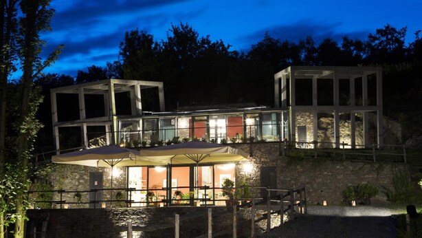 A modern building with multiple levels, outdoor seating, and a stone facade. - Agriturismo Rossolampone (San Bernardino Verbano)