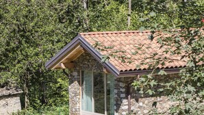 A stone building with a tiled roof, large windows, and a small garden area with a bench and a white towel. - Agriturismo Rossolampone (San Bernardino Verbano)
