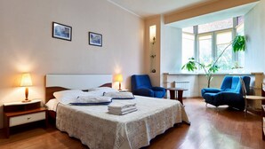 A hotel room with a bed, two chairs, a small table, and a window with plants. - Home-Hotel Voloshskaya 51 (Kyiv)