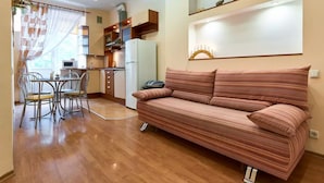 A cozy living room with a sofa, a dining table with chairs, a kitchen area with cabinets and appliances, and a window with curtains. - Home-Hotel Voloshskaya 51 (Kyiv)