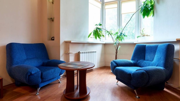 A room with two blue armchairs, a small wooden table, and a large window with plants. - Home-Hotel Voloshskaya 51 (Kyiv)